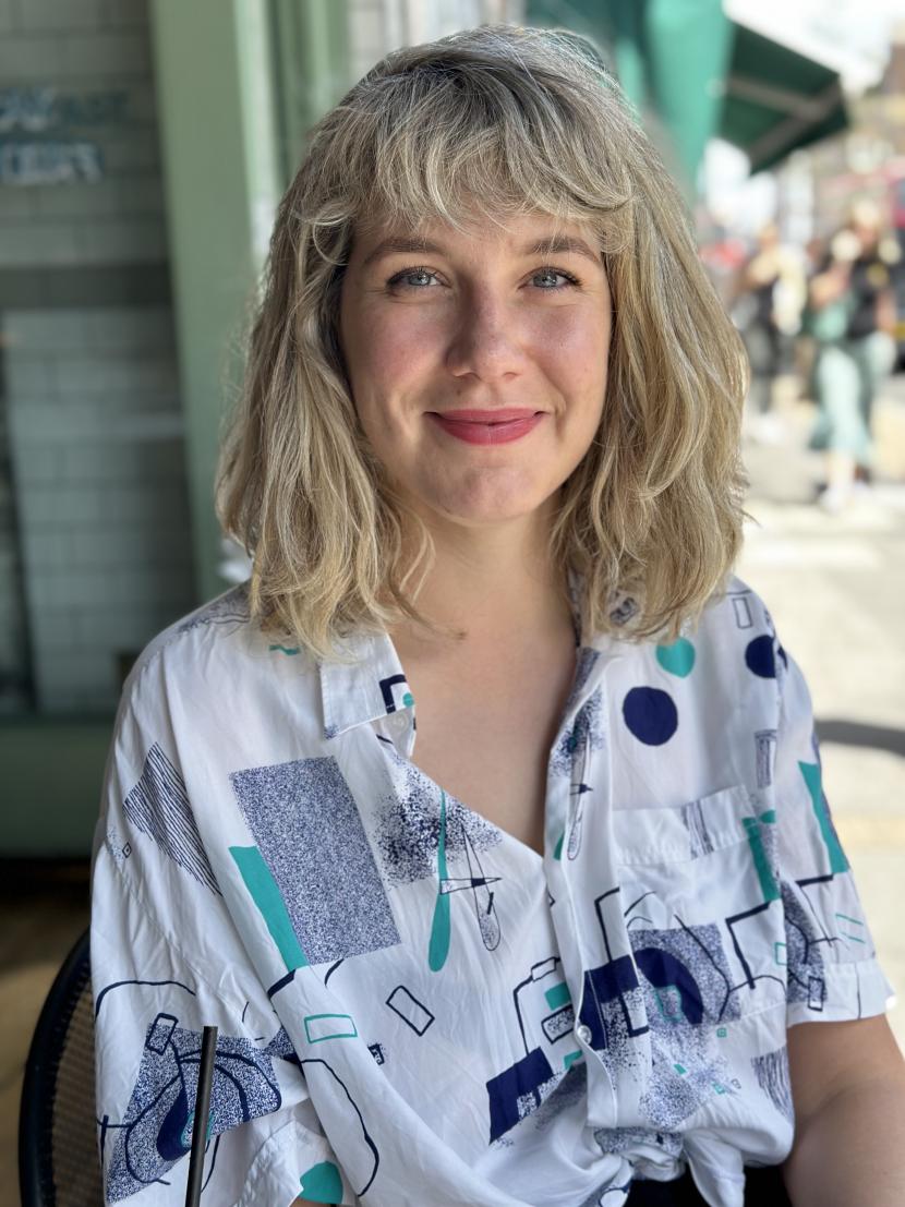 Een foto van Paula Bogutyn. Haar blonde haren zijn in een pony geknipt en komen tot op schouderlengte. Ze draagt een witte blouse met verschillende blauwgroene kubistische vormen op. 