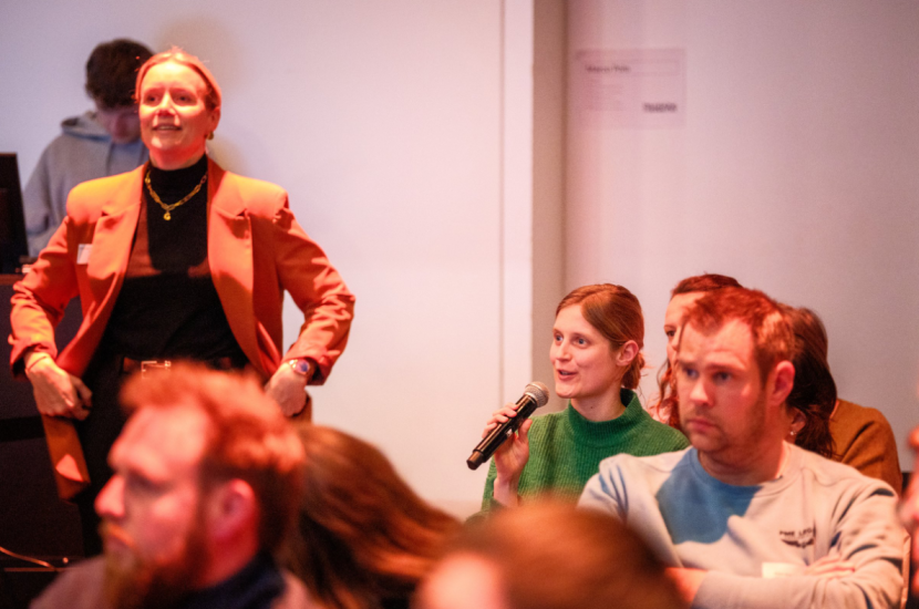 Een foto van Hanne van Symfoon die in het publiek een vraag stelt in een microfoon.