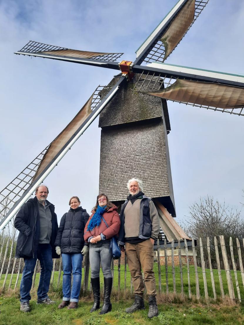 Een foto van Francis, Léticia en Jo die poseren voor een molen, samen met molenaar Erik.