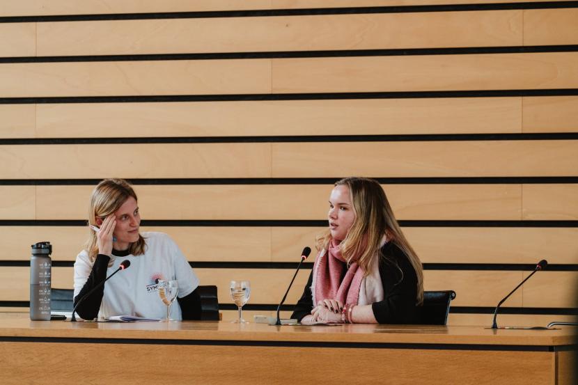 Een foto van Hanne van Symfoon en vrijwilligster Leontien op Met het Oog op Symfoon 2025. Ze zitten vooraan en spreken het publiek toe.