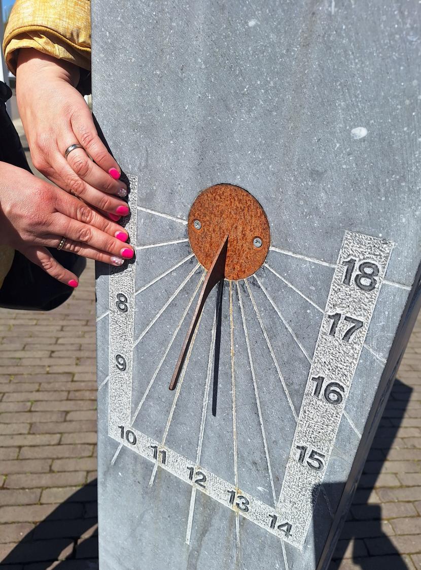 Twee handen voelen aan de reliëfelementen van een stenen zonnewijzer in Klingspoor.
