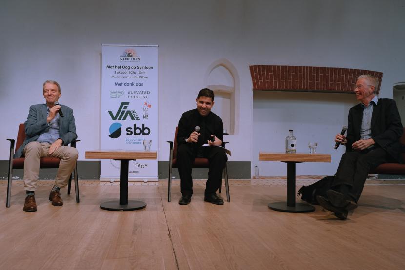 Johan Decaluwé, moderator Youssri Mejdoubi en Jan Hautekiet zitten naast elkaar vooraan. De drie heren lachen.
