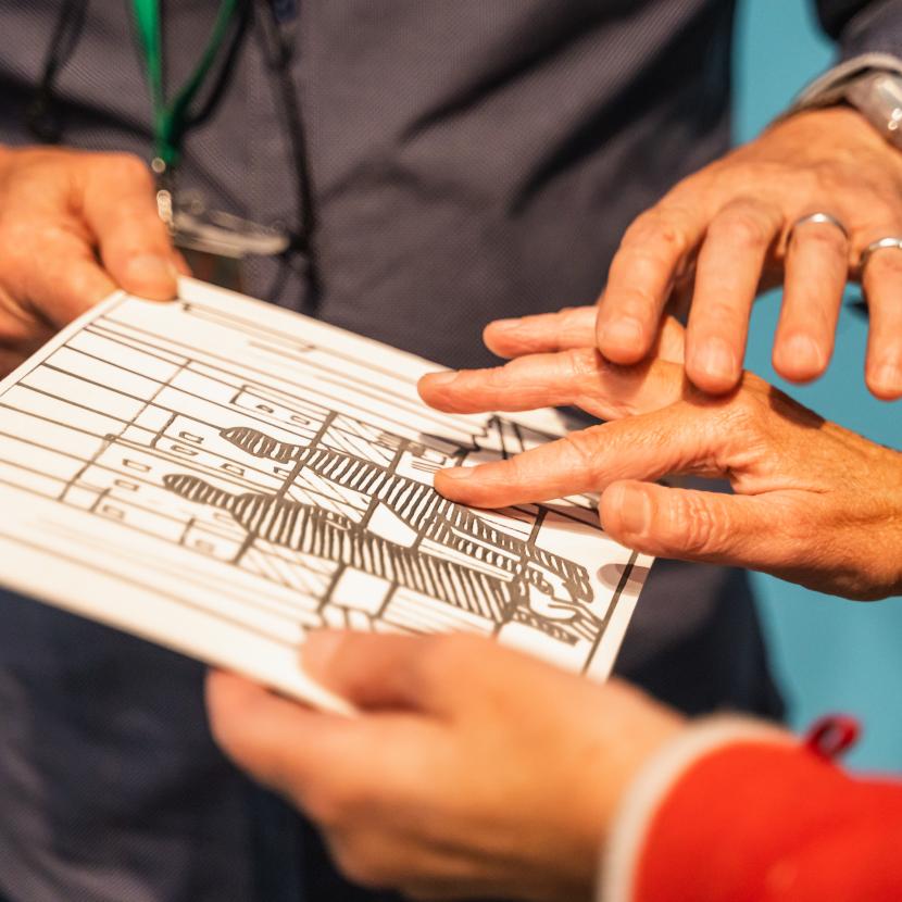 De gids houdt een voelplaat op zwelpapier vast en legt de hand van een bezoeker op de juiste plaats op de voelplaat.